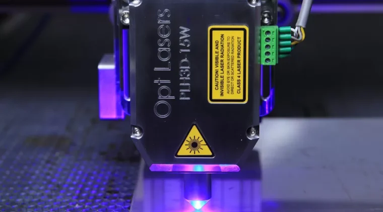 CNC işleme merkezinde, lazer teknolojisiyle entegre edilmiş bir makine, metal parça üzerinde hassas kesim işlemi gerçekleştiriyor.